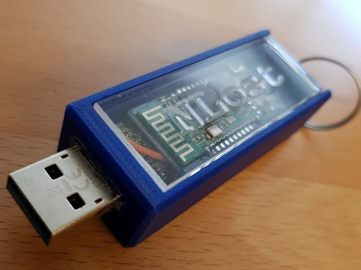 The NLost prototype: a USB stick in a 3D-printed blue case with a Bluetooth module visible through a clear window, on a wooden desk